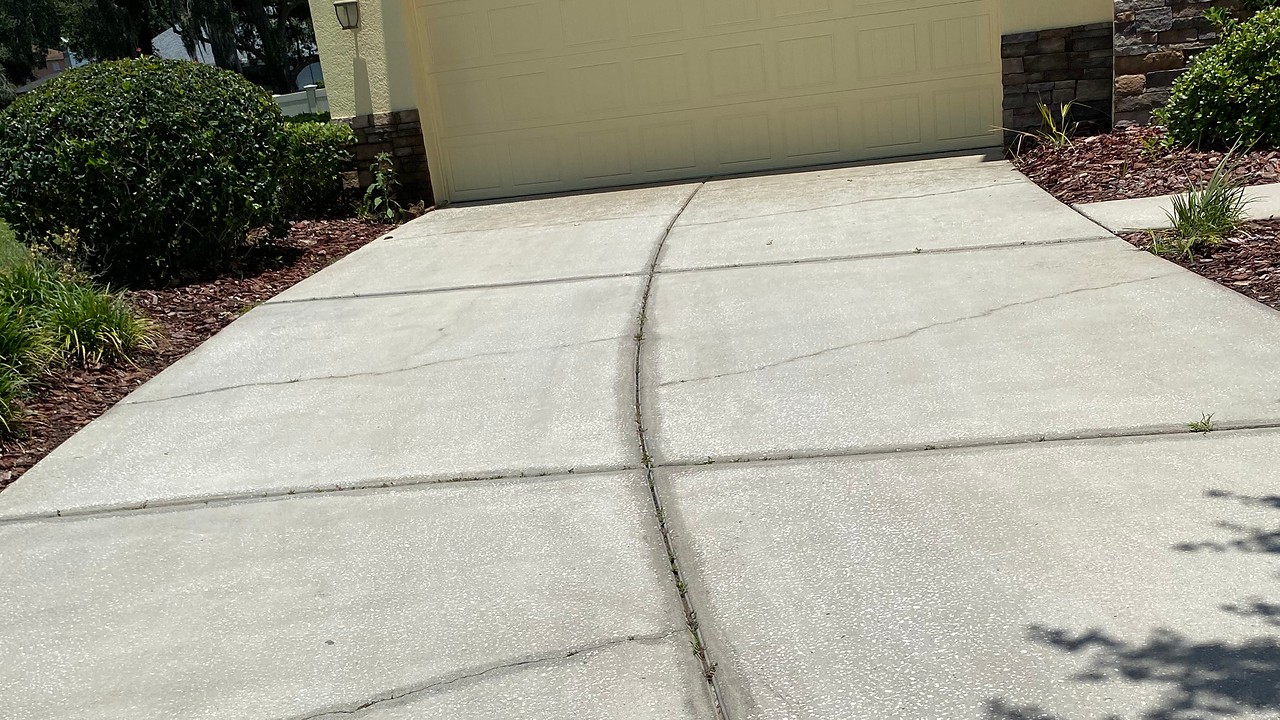 Driveway after cleaning, with the concrete visibly lighter while existing cracks remain.