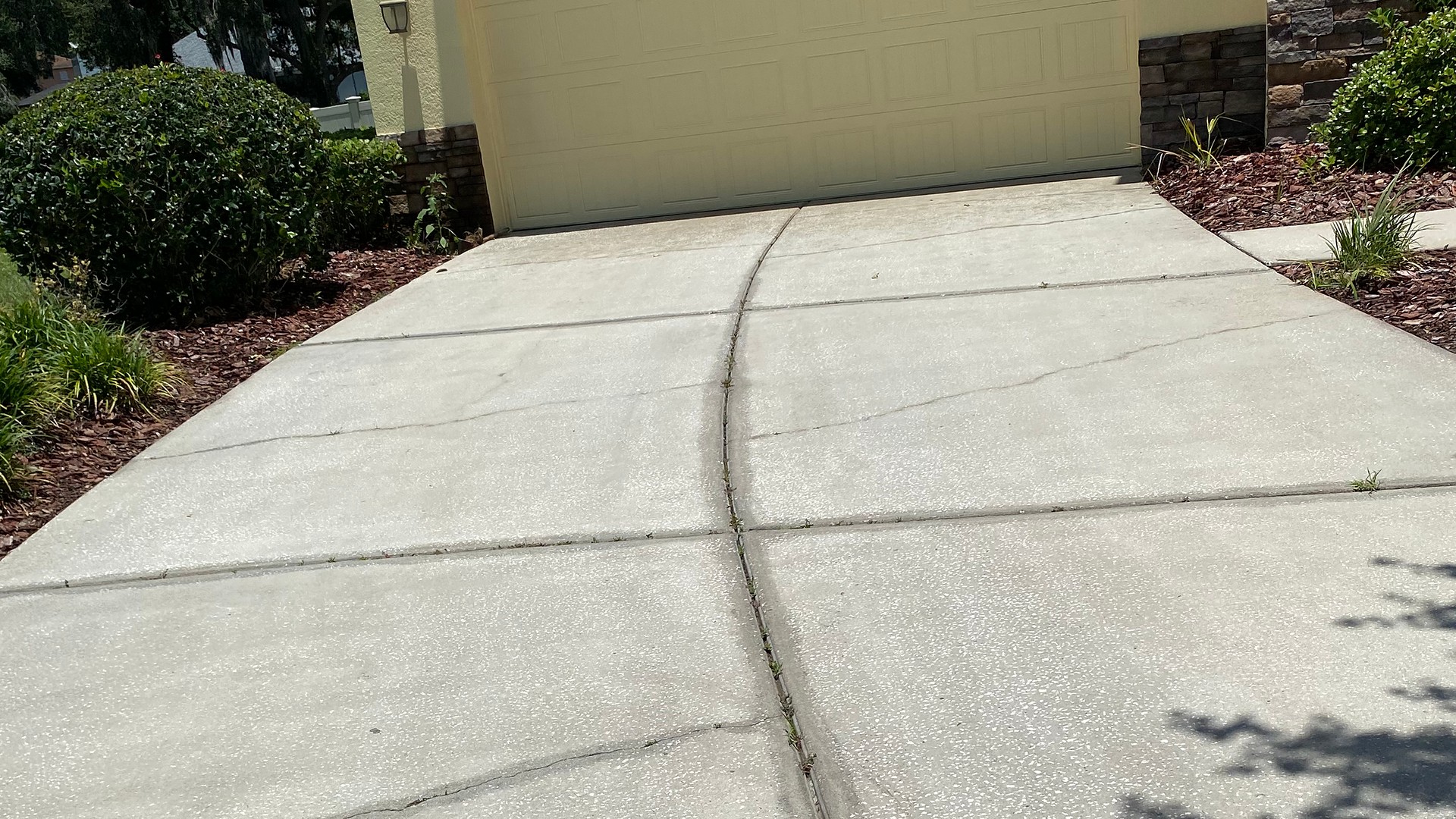 The same driveway after exterior cleaning, with the concrete visibly lighter while existing cracks remain.