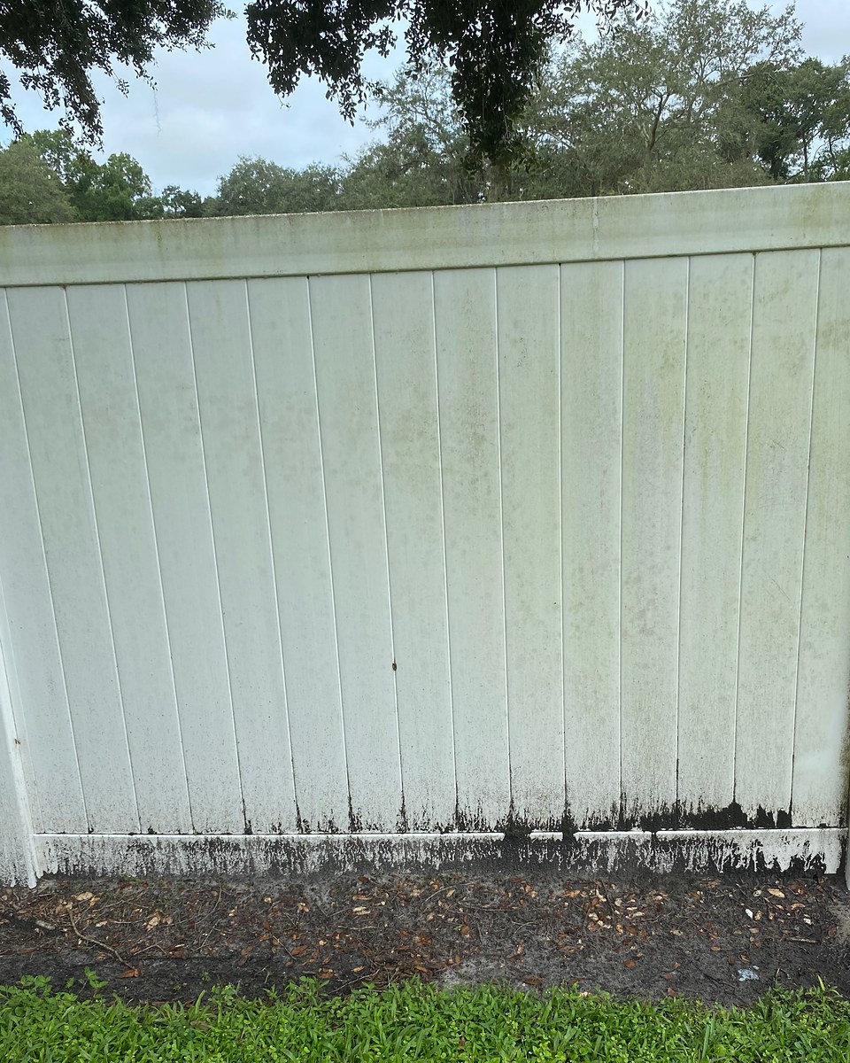 White vinyl fence panel with algae and dark buildup along the lower edge before cleaning.